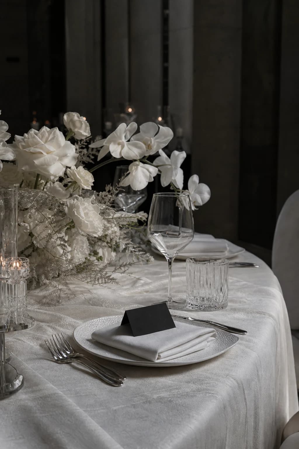 Ivory wedding table with white orchids, crystal glassware, and black place card